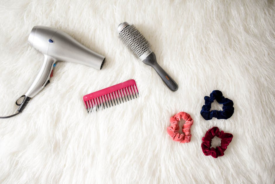 Flatlay of hairstyling tools including a hairdryer, brush, comb, and scrunchies on white fur