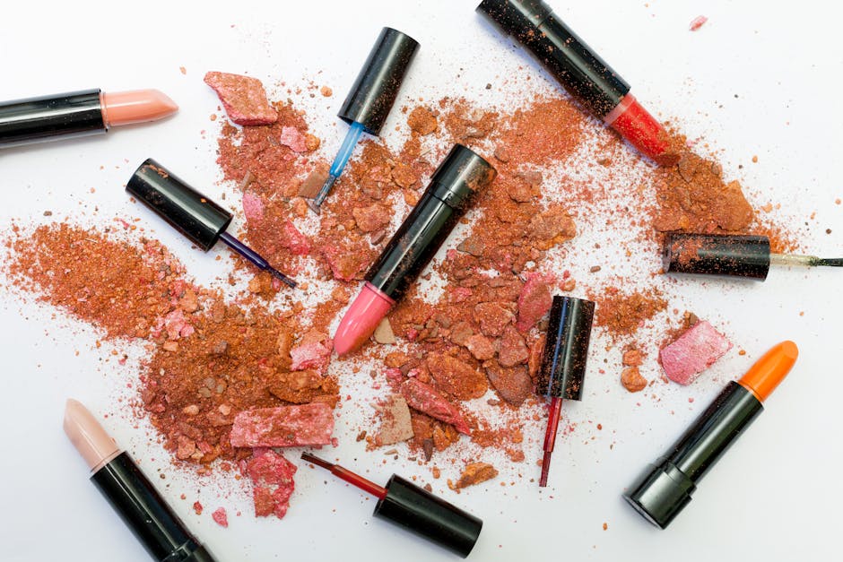 Colorful scattered makeup products including lipsticks and crushed powders on a white background