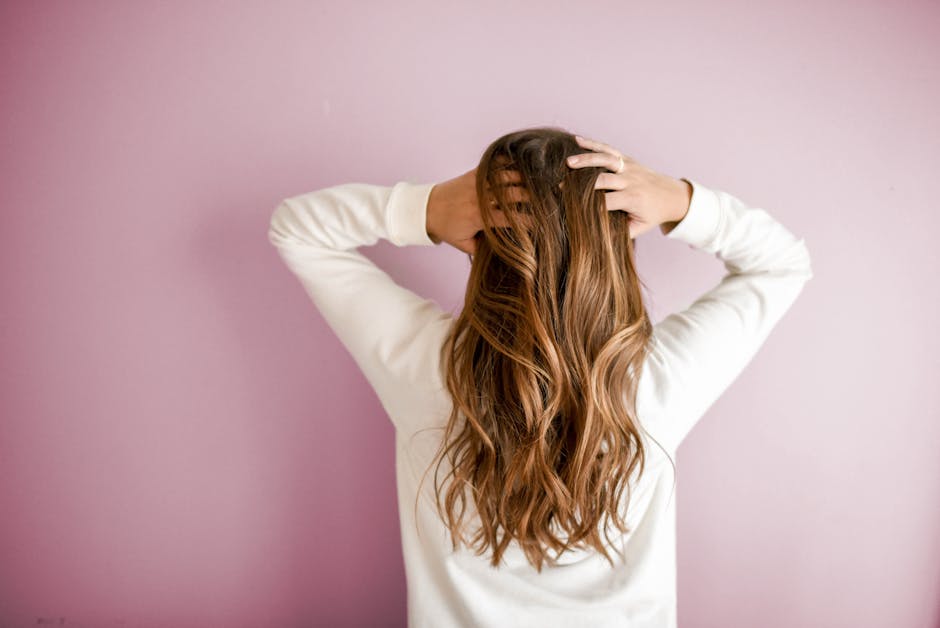 Back view of a woman with elegant long brown hair against a pink wall, showcasing stylish hair design